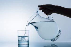 Cropped image of woman pouring water from transparent jug into glass