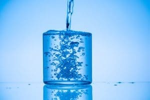 toned image of water pouring in full glass on blue background